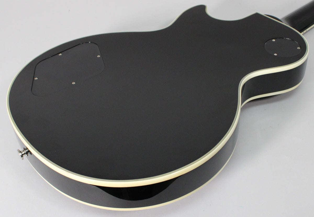 The back of the glossy black Les Paul Custom, showing the control cavity and switch access plates, with cream binding around the body.