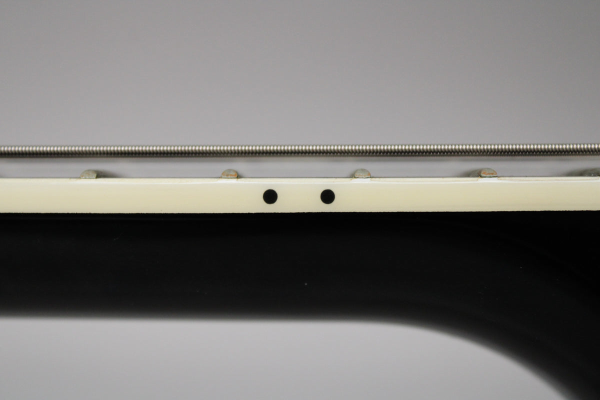 Close-up of the guitar's cream binding and black fretboard, showing two small black dots and a single wound string.