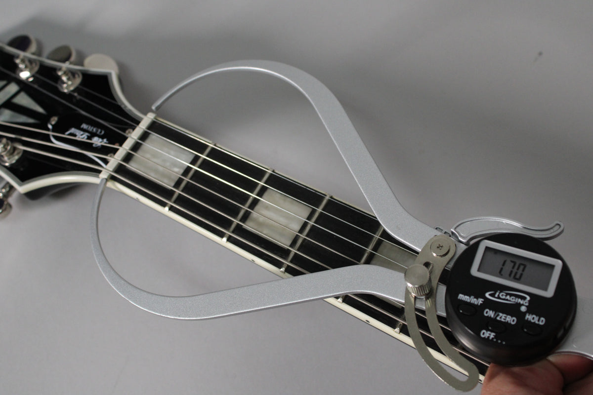 A digital caliper measures the nut width of the black headstock and fretboard with rectangular pearloid inlays.