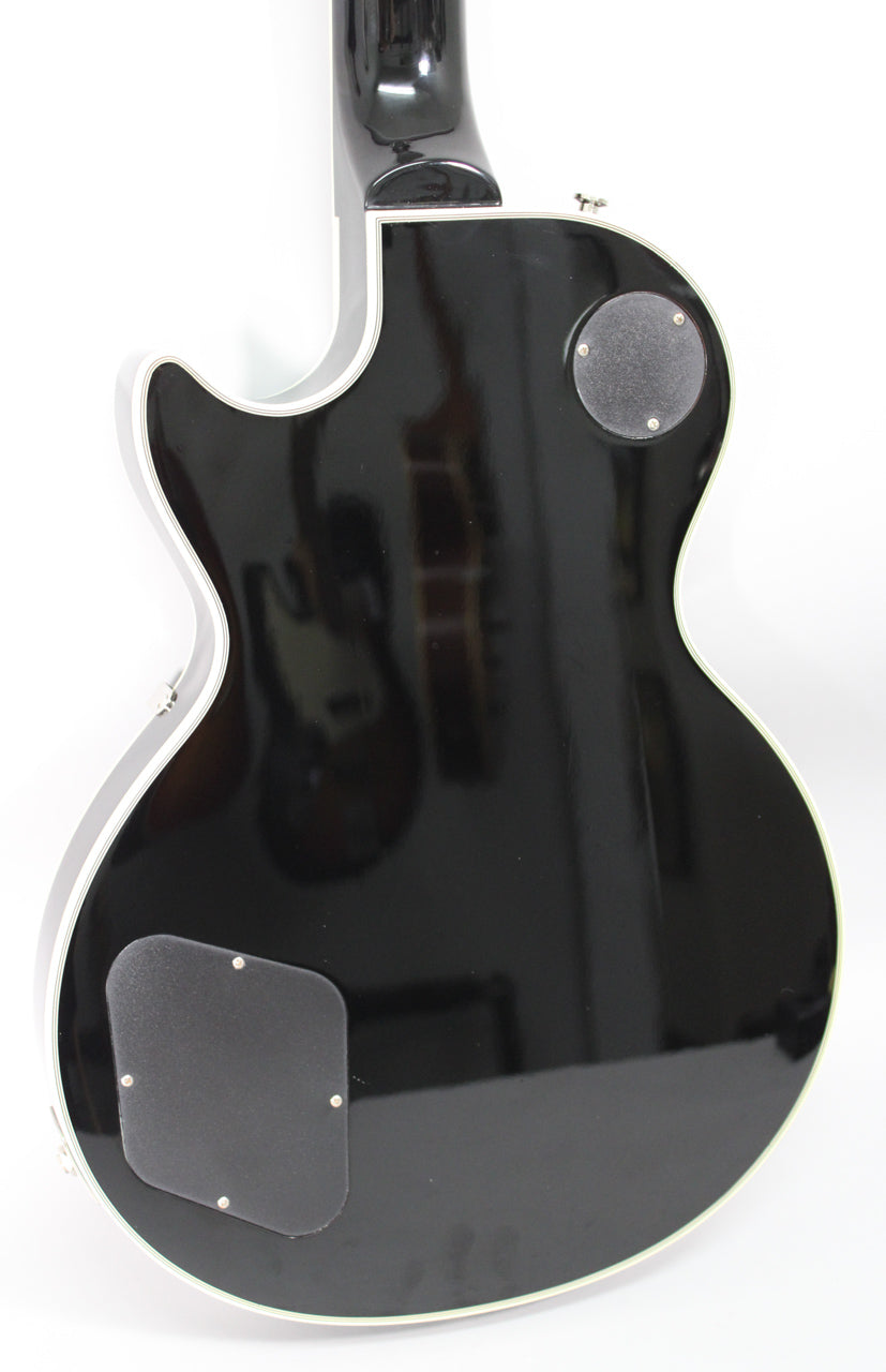 The back of a black Les Paul Custom, showing the neck joint, control cavity, and jack plate, all with white binding.