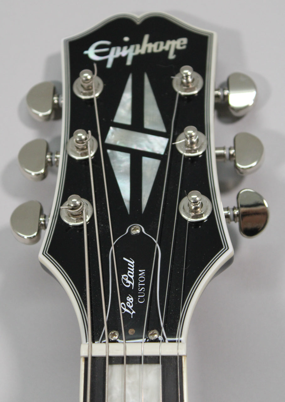 The black headstock, with white binding and mother-of-pearl inlays, is angled slightly down, showing six chrome tuners.