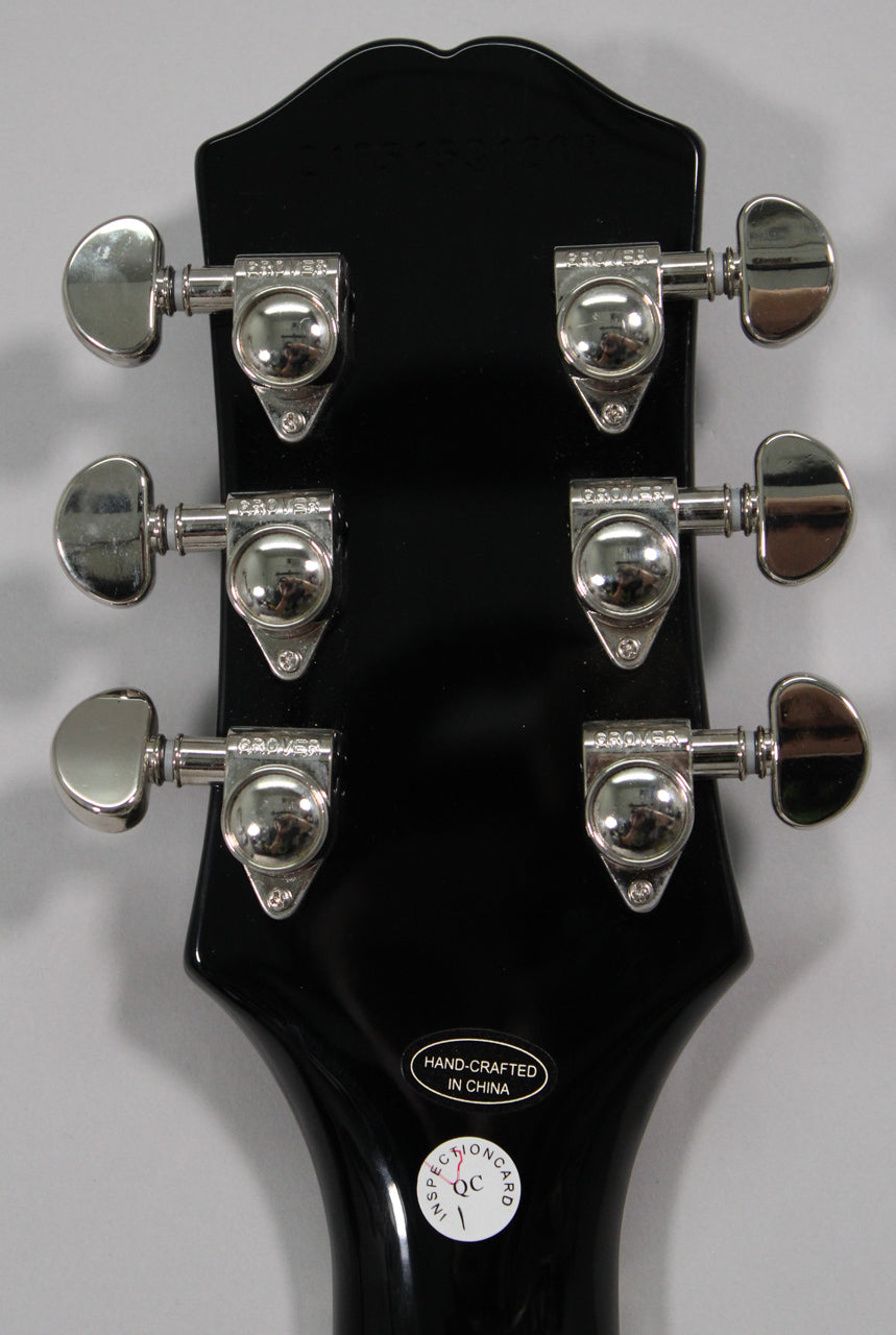The back of a glossy black headstock with six chrome tuners, three on each side, and two white stickers near the neck joint.