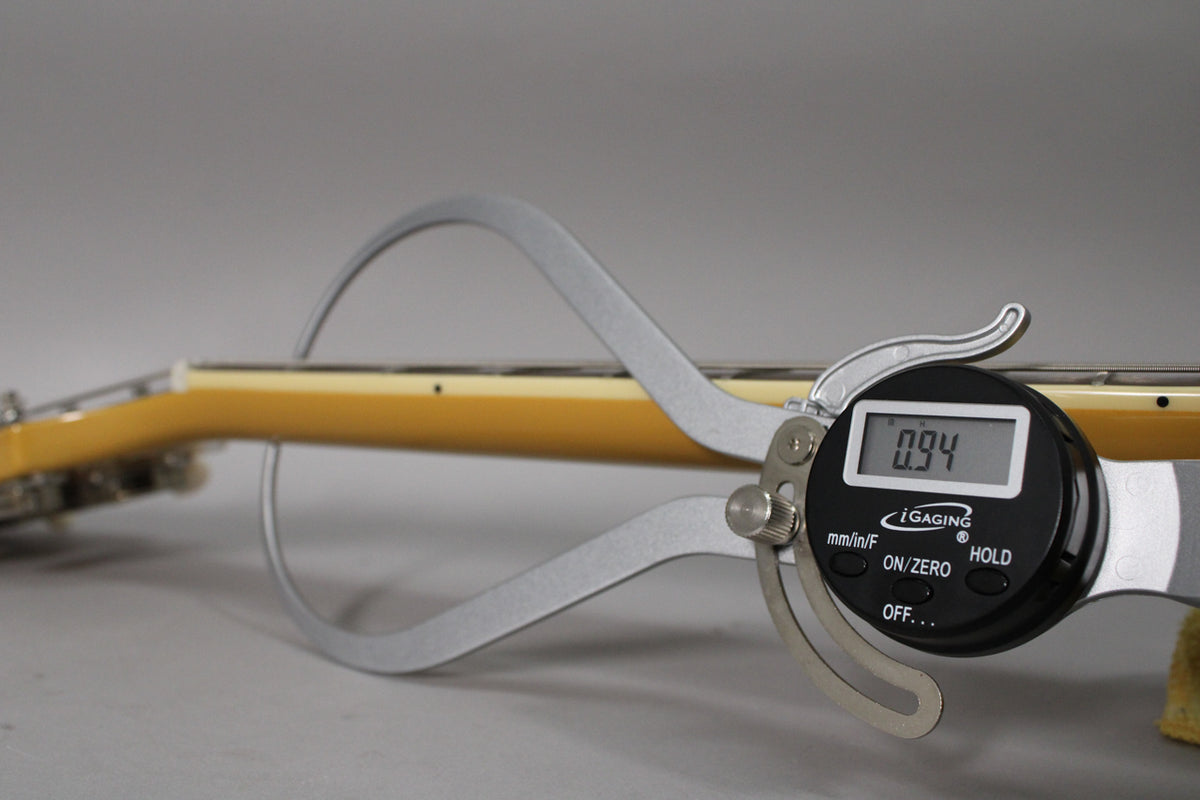 A digital caliper measures the guitar's neck thickness at 0.94 inches, showing the TV Yellow finish and fretboard binding.