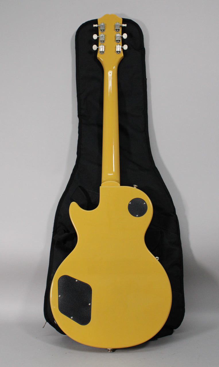 The back of a glossy TV yellow guitar with a black control cavity cover and a black gig bag behind it.
