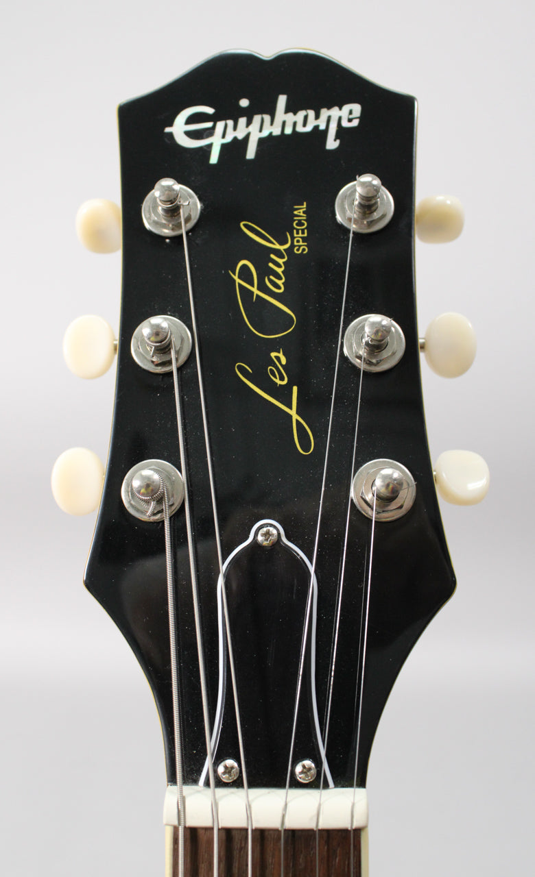 Close-up of the black gloss headstock, showing six cream tuning pegs, silver string posts, and the top of the fretboard.