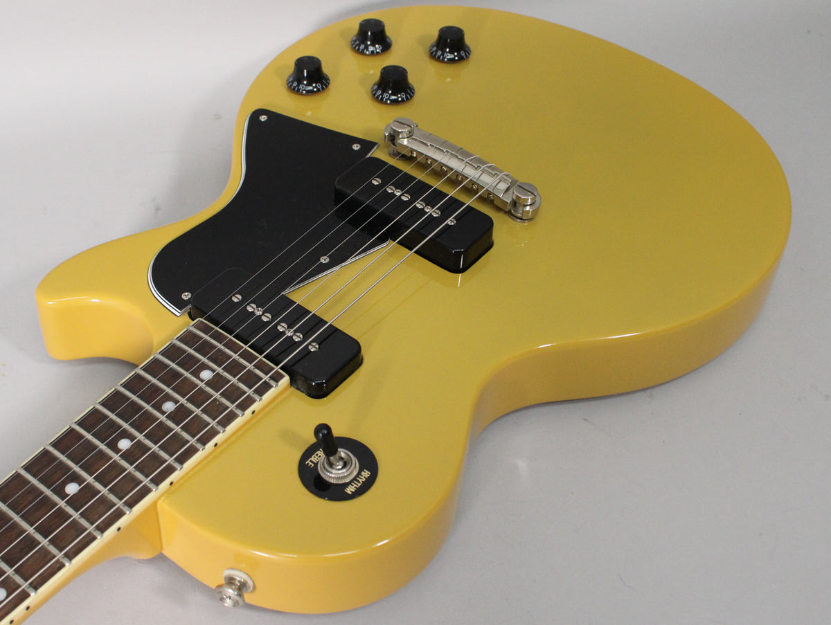 Close-up of a glossy TV yellow guitar body with black pickguard, two P90 pickups, a bridge, and four black control knobs.