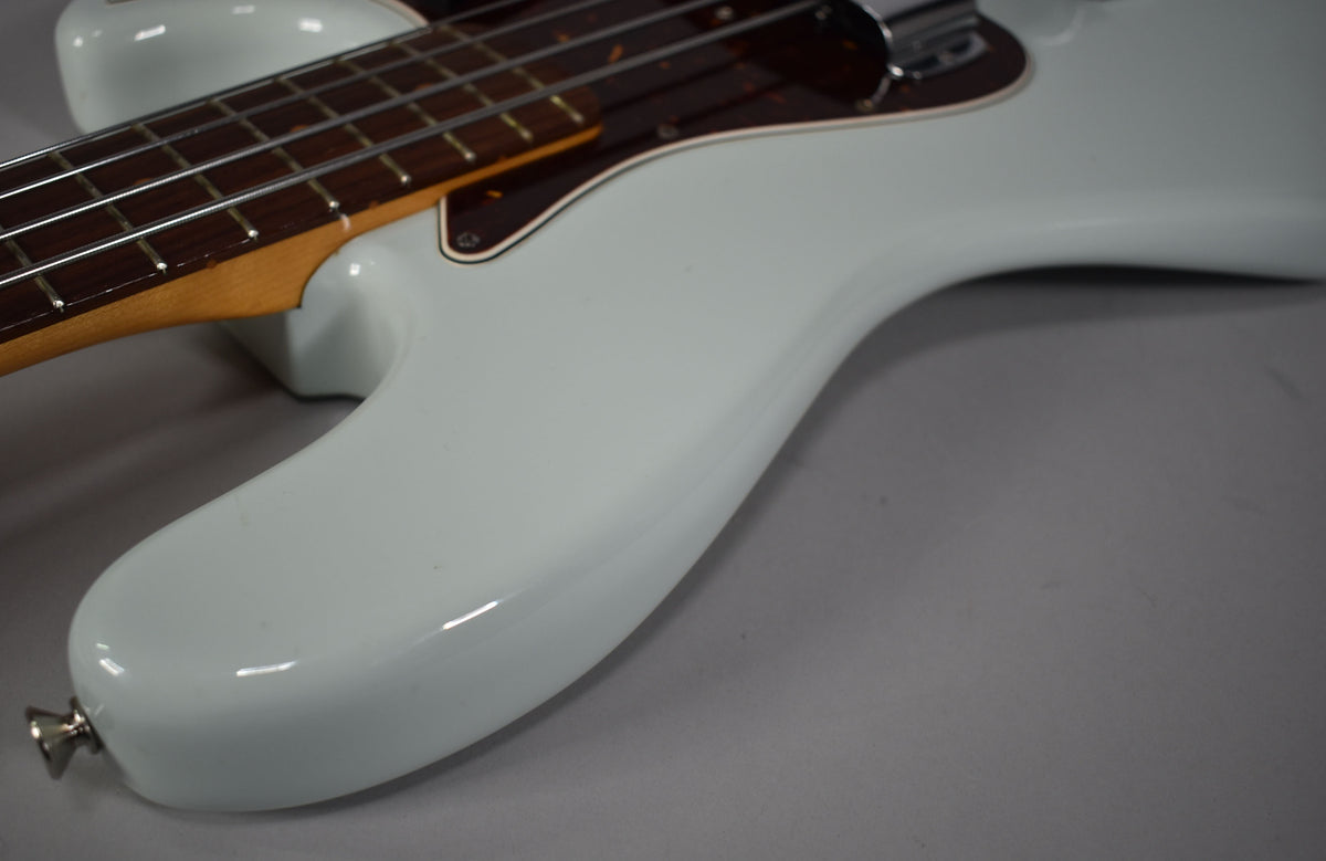 The upper body of a light blue bass, with a dark brown pickguard and rosewood fretboard, is angled from the lower left.