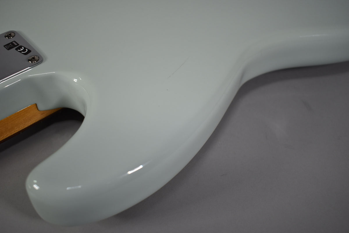 Close-up of the bass's glossy sonic blue body, showing the neck joint and a faint scratch on the upper bout.