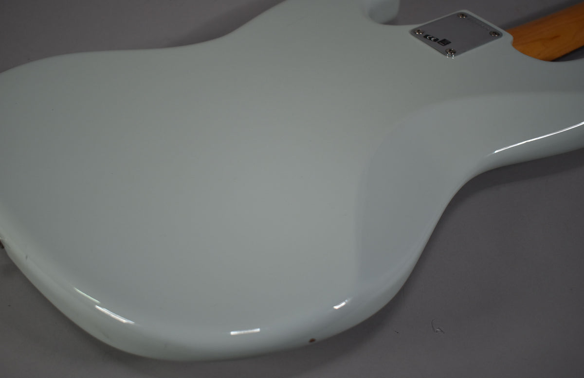 The bass's glossy sonic blue body is shown from the back, with a chrome neck plate and a small chip near the bottom edge.