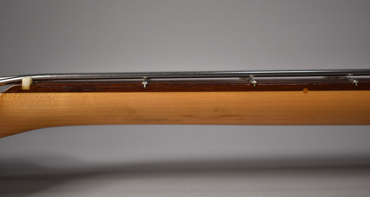 Close-up of the bass neck from the side, showing the light maple wood, dark rosewood fretboard, and four metal strings.