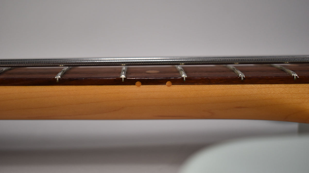 Close-up of the bass neck from the side, showing the dark rosewood fretboard, light maple neck, and two round side dot markers.