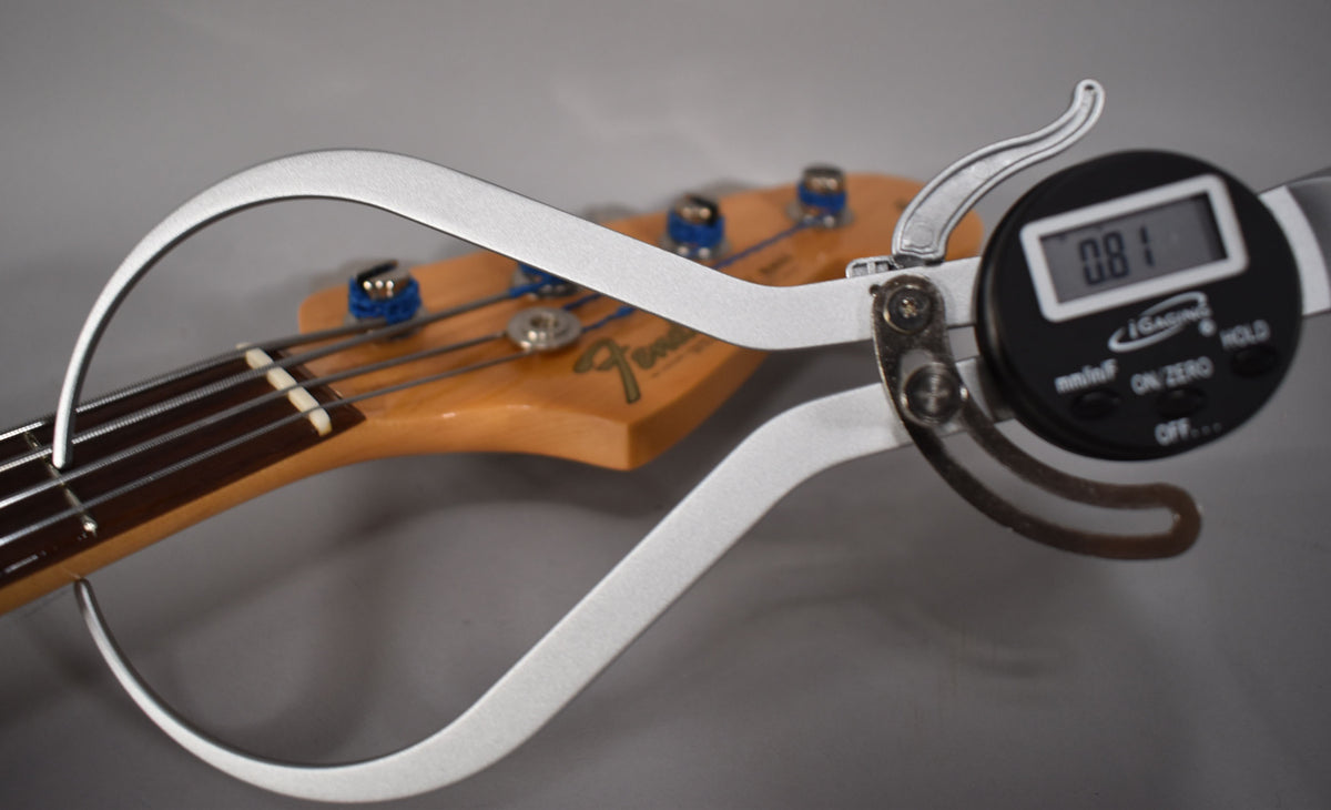 A digital caliper measures the bass's fretboard radius, showing "0.81" on its display, with the headstock blurred in the background.