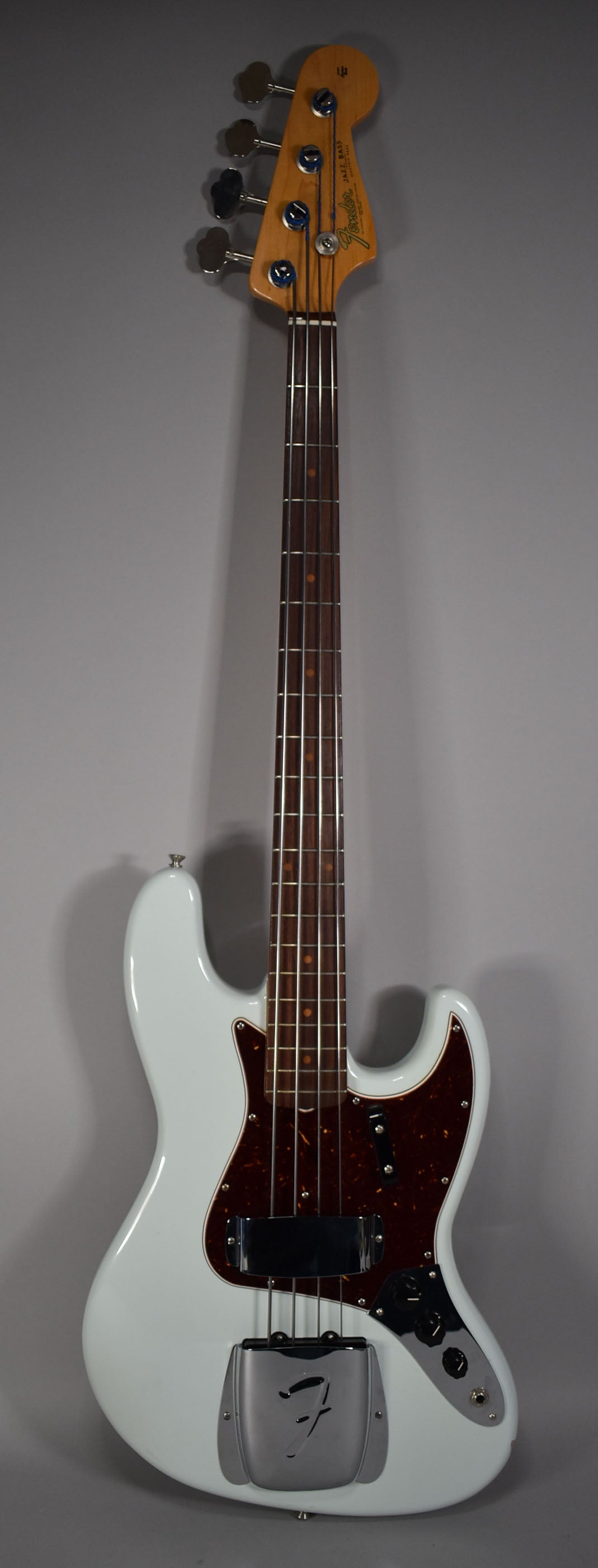 Full-length view of a light blue bass with a tortoiseshell pickguard, chrome bridge cover, and dark rosewood fingerboard.