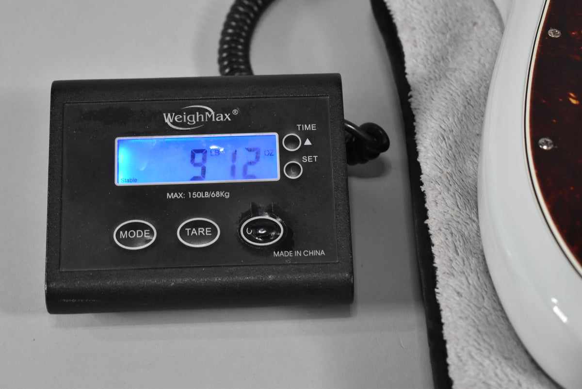 A digital scale displays "9 LB 12 OZ" next to the Sonic Blue bass body with a tortoiseshell pickguard.