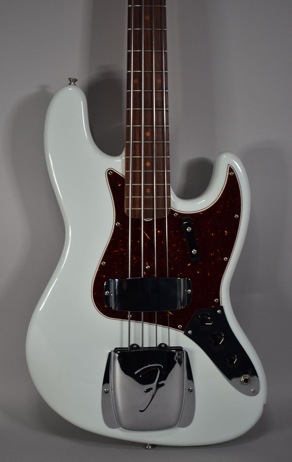 Upper body of a sonic blue bass with a tortoiseshell pickguard, chrome bridge cover, and black control knobs.