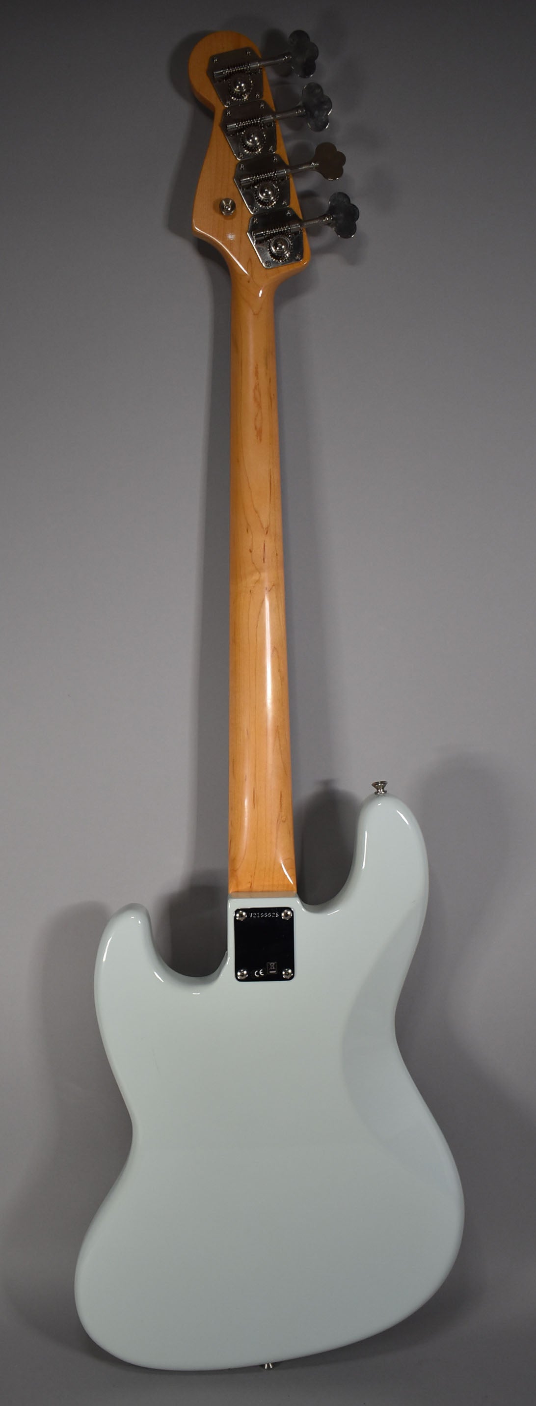 The back of a light blue bass guitar with a glossy finish, showing the maple neck and headstock with four chrome tuners.