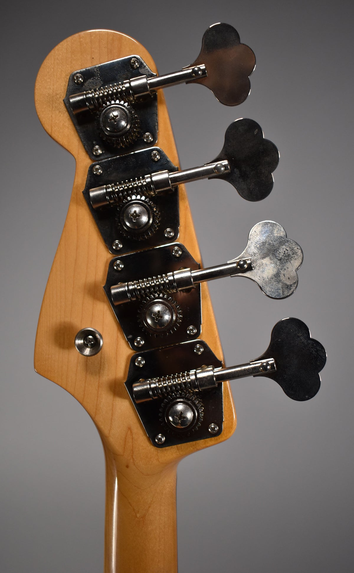Close-up of the bass headstock and upper neck, showing four clover-leaf tuners with tarnished chrome hardware.