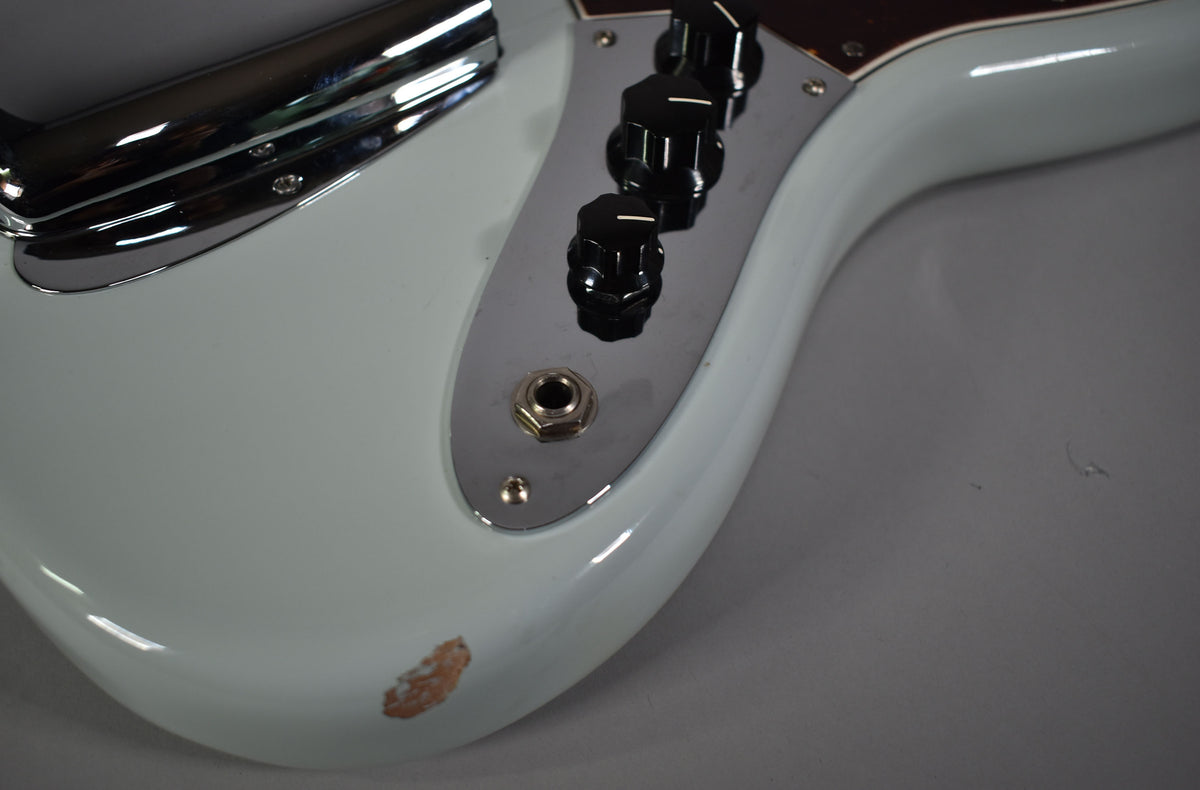 Close-up of the bass's lower body, showing the light blue finish, chrome control plate with three black knobs, and a chip revealing wood.