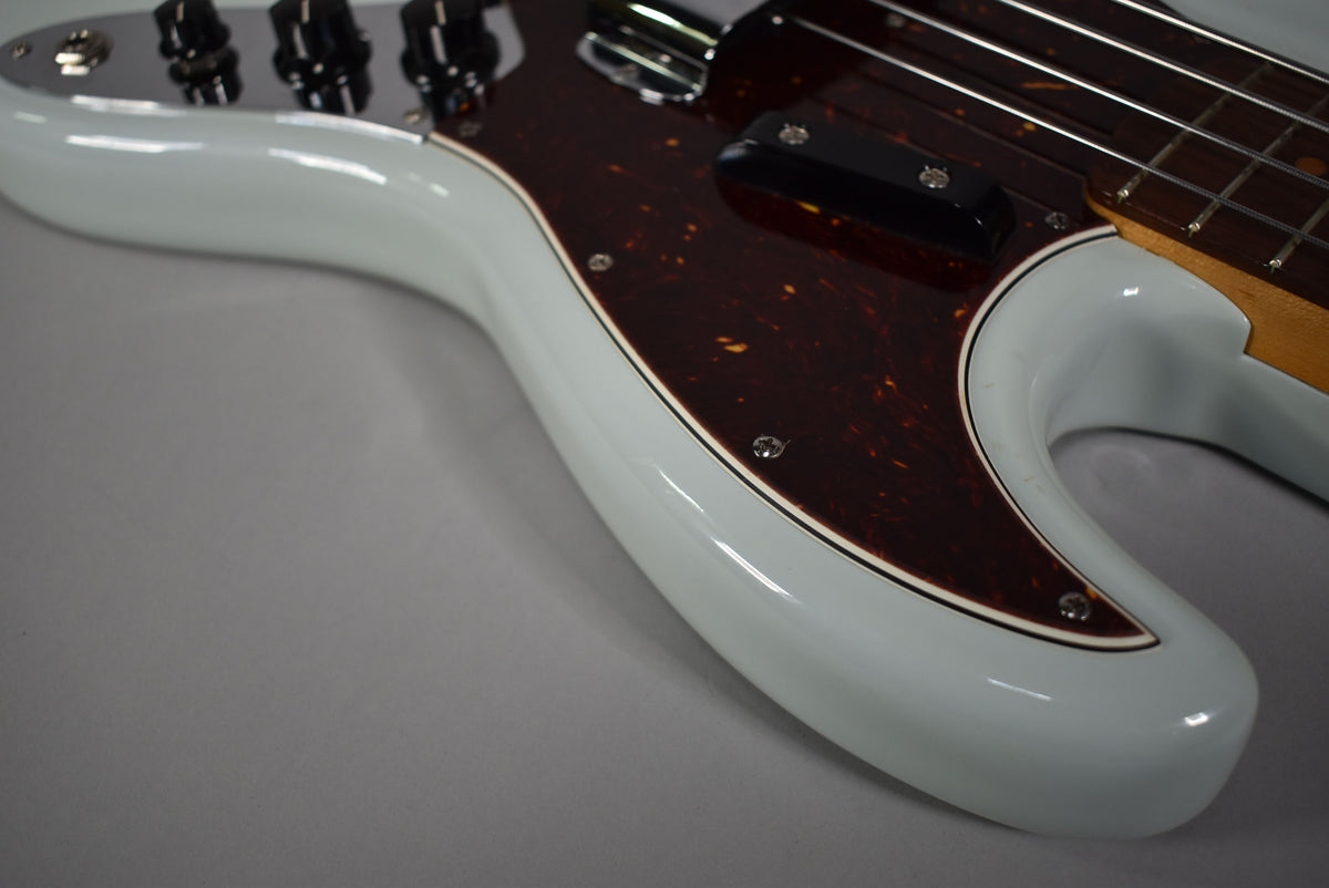 Close-up of the bass's upper body, showing the glossy sonic blue finish, tortoise pickguard, chrome control plate with black knobs, and neck pickup.