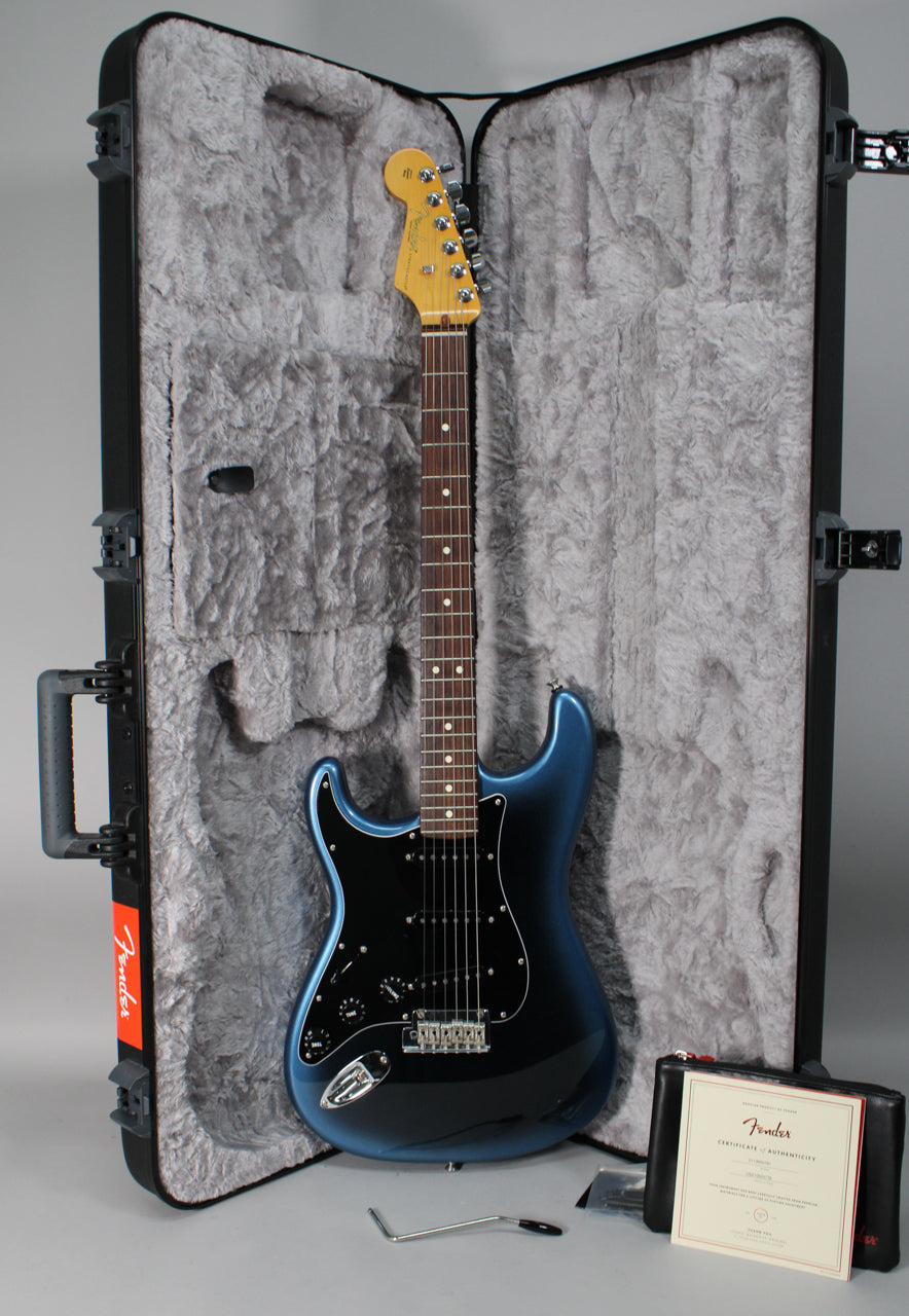 A left-handed Stratocaster in a dark blue burst finish with a black pickguard, shown in its open, grey-lined hard case.
