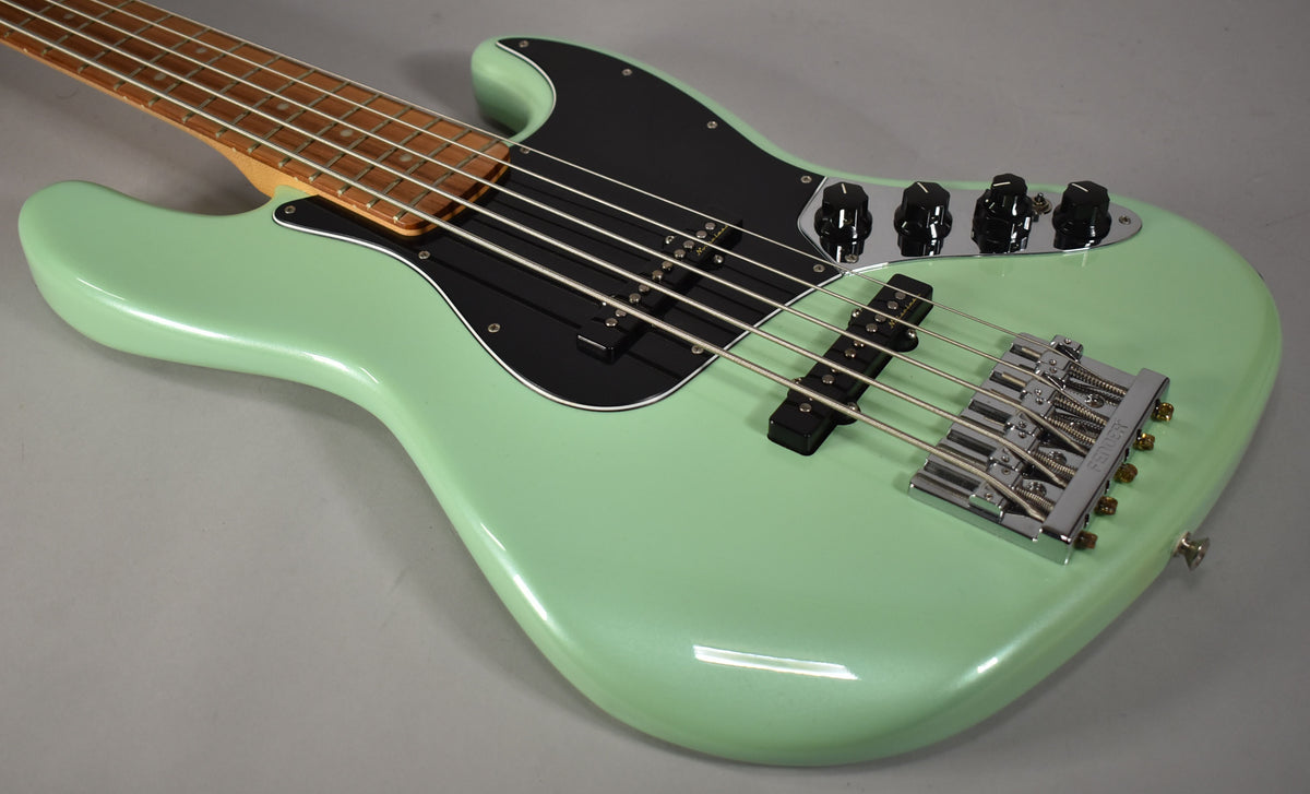 The mint green bass guitar, with a black pickguard and chrome hardware, is angled from the upper left, showing the body and neck.