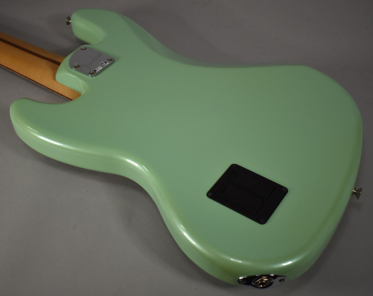 The bass guitar's back, in glossy surf pearl, shows a chrome neck plate, a black rectangular control cavity cover, and a strap button.