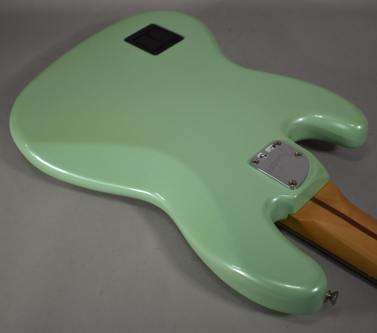 The bass guitar's back is shown in Surf Pearl green, with a black rectangular battery cover and a chrome neck plate.