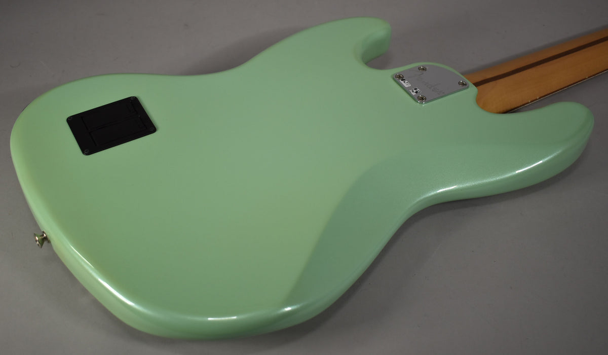 The back of a mint green bass guitar, showing the neck plate, battery compartment, and lower strap button.
