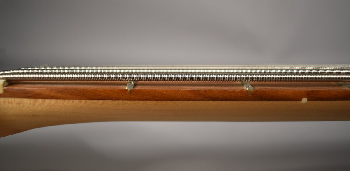 Close-up of the bass's neck and fretboard from the side, showing the five strings, frets, and a light-colored side dot.