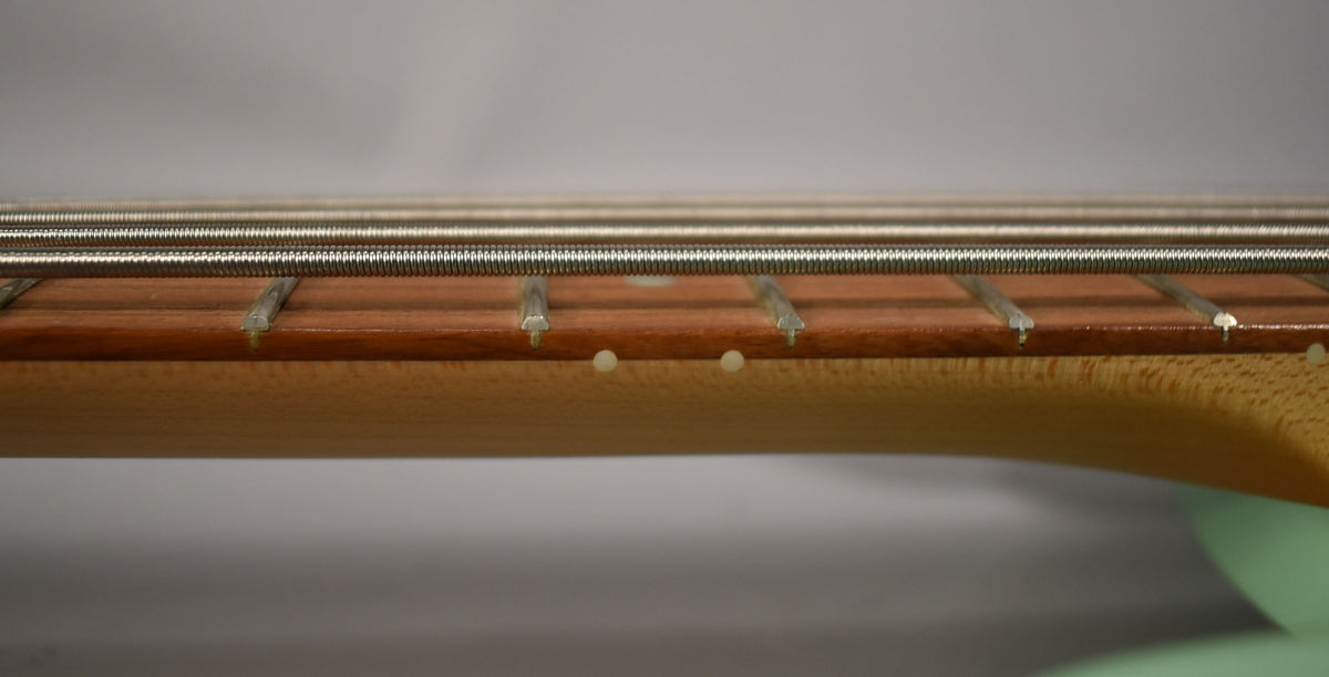 Close-up of the bass neck and fretboard from the side, showing five strings, frets, and two white side dot markers.