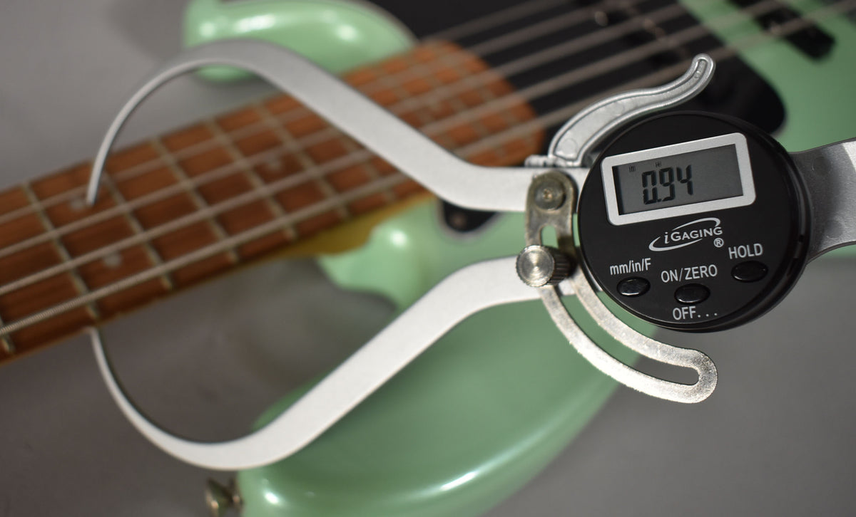 A digital caliper measures the string height at the 12th fret of the surf pearl bass, showing 0.94mm.