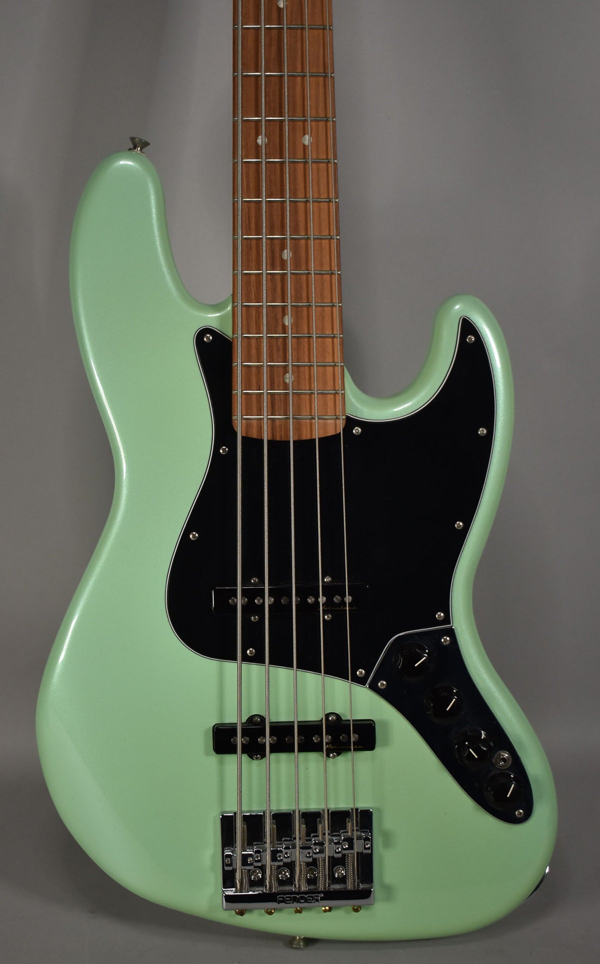 A 5-string bass in Surf Pearl green, angled to show the body, black pickguard, chrome bridge, and dark fretboard.
