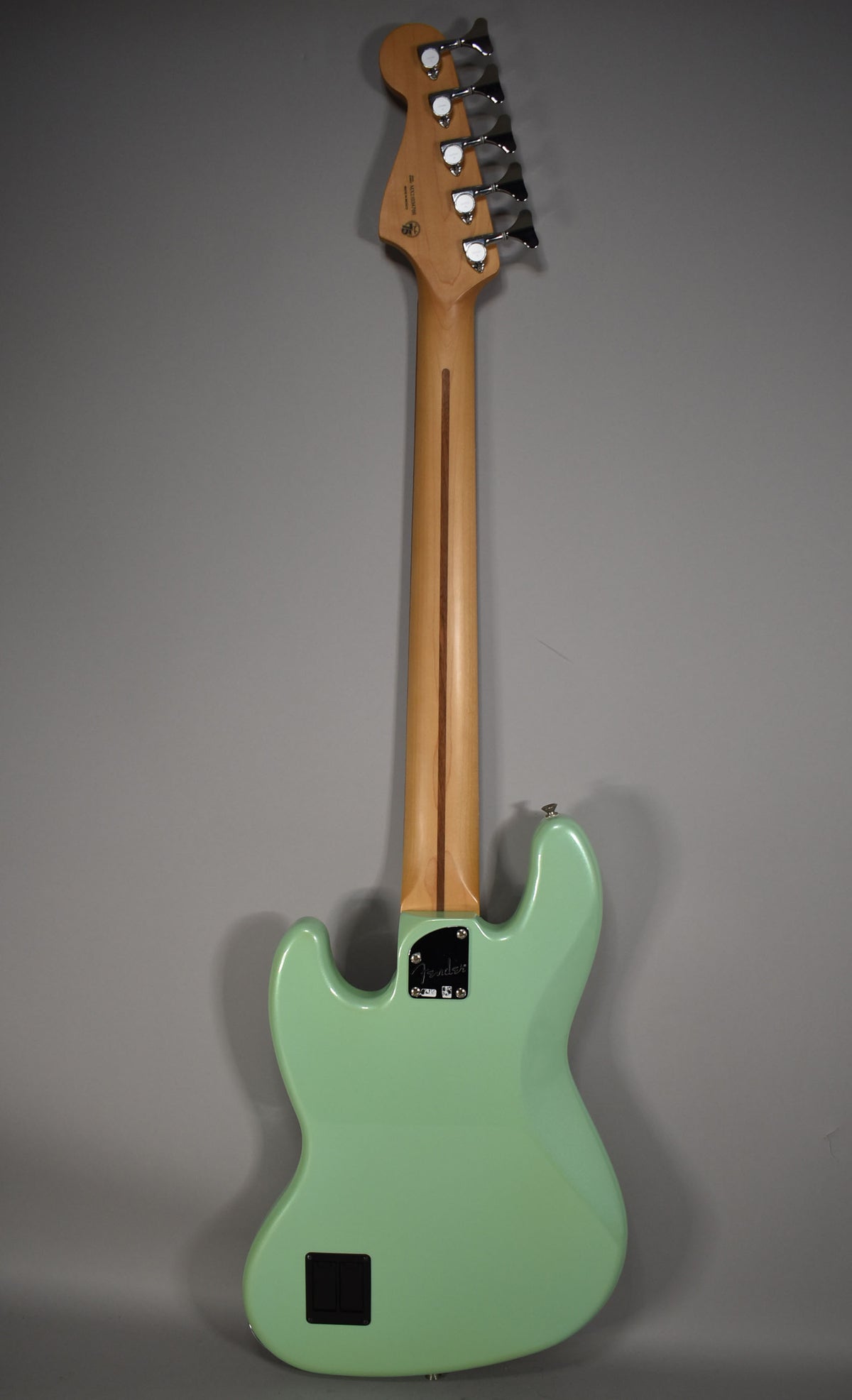 Rear view of a Surf Pearl green bass, showing its maple neck with a dark stripe, 5 chrome tuners, and a black battery compartment.