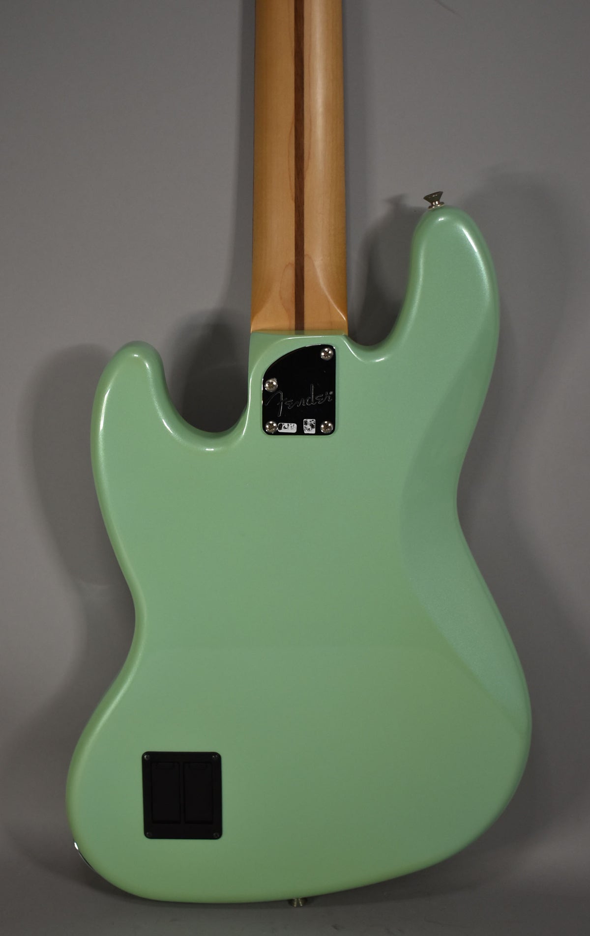 Rear view of a Surf Pearl green bass, showing the light wood neck, black neck plate, and rectangular battery compartment.