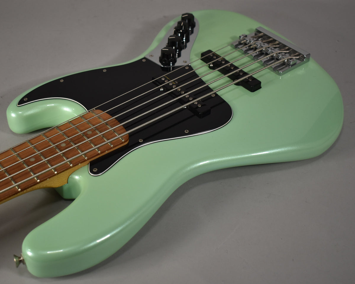 The bass body in Surf Pearl finish, with a black pickguard, chrome bridge, and five strings, is angled from the lower bout.