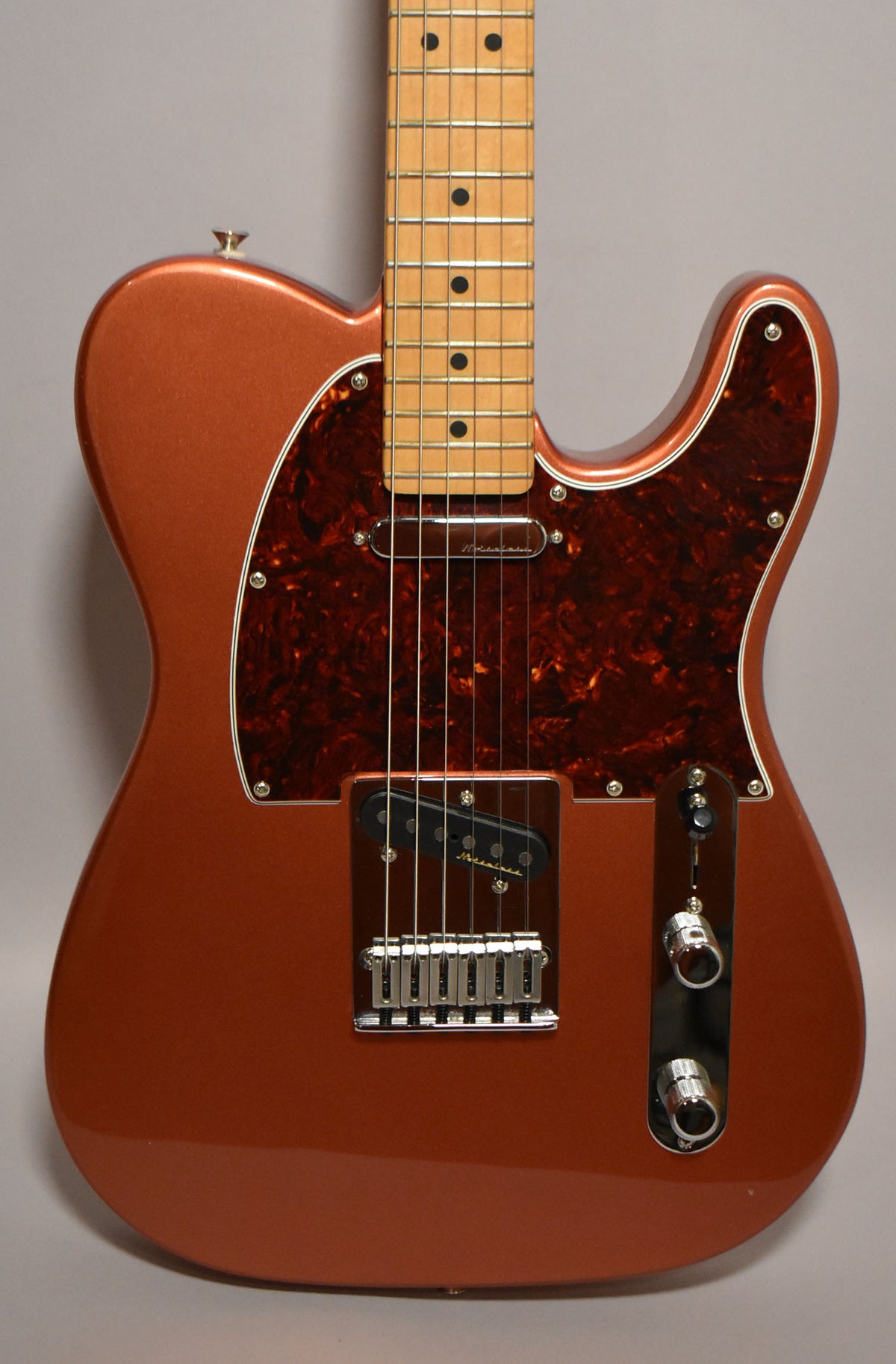 A metallic candy apple red Telecaster, framed from the waist up, with a tortoiseshell pickguard and maple fretboard.