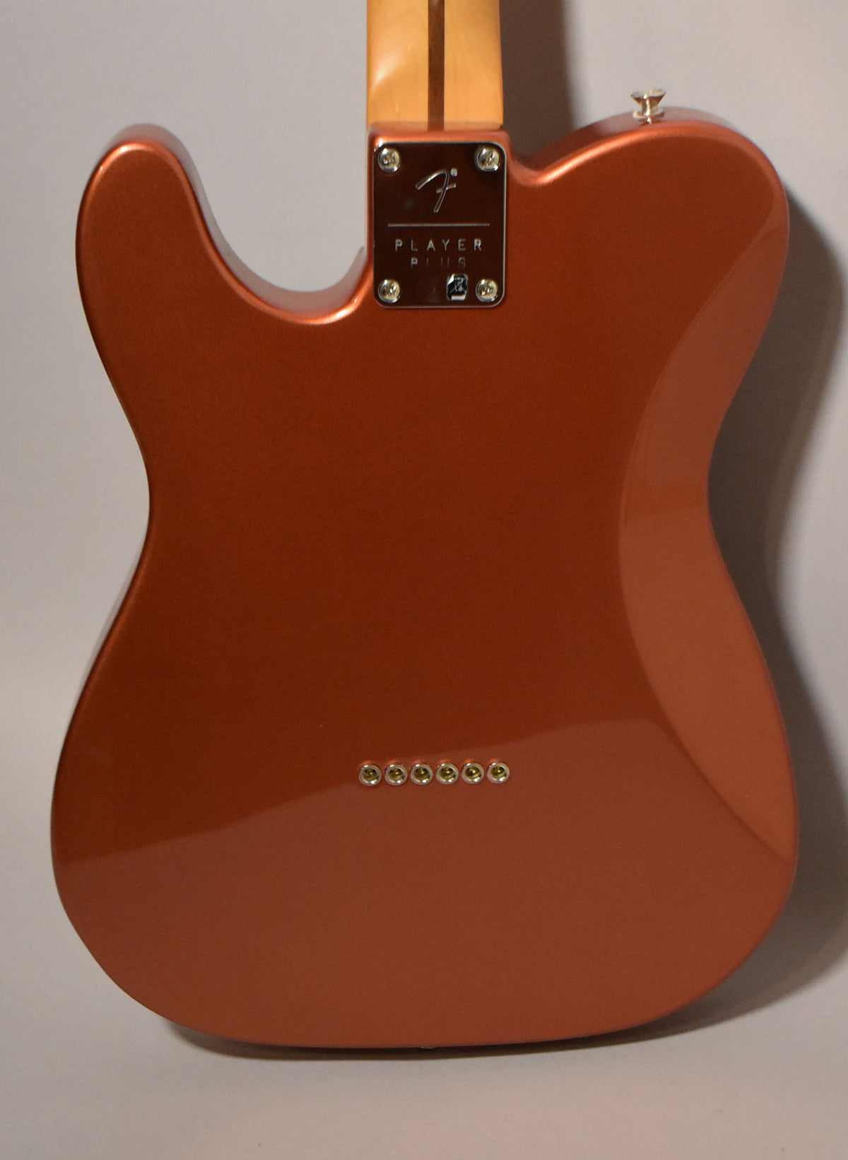 The back of a metallic candy apple red Telecaster body, showing the neck plate, strap button, and six string ferrules.