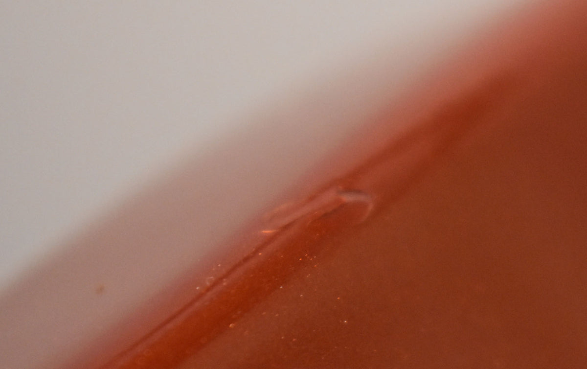 Close-up of a small, clear chip in the glossy Candy Apple Red finish on the guitar's body, revealing a lighter layer underneath.