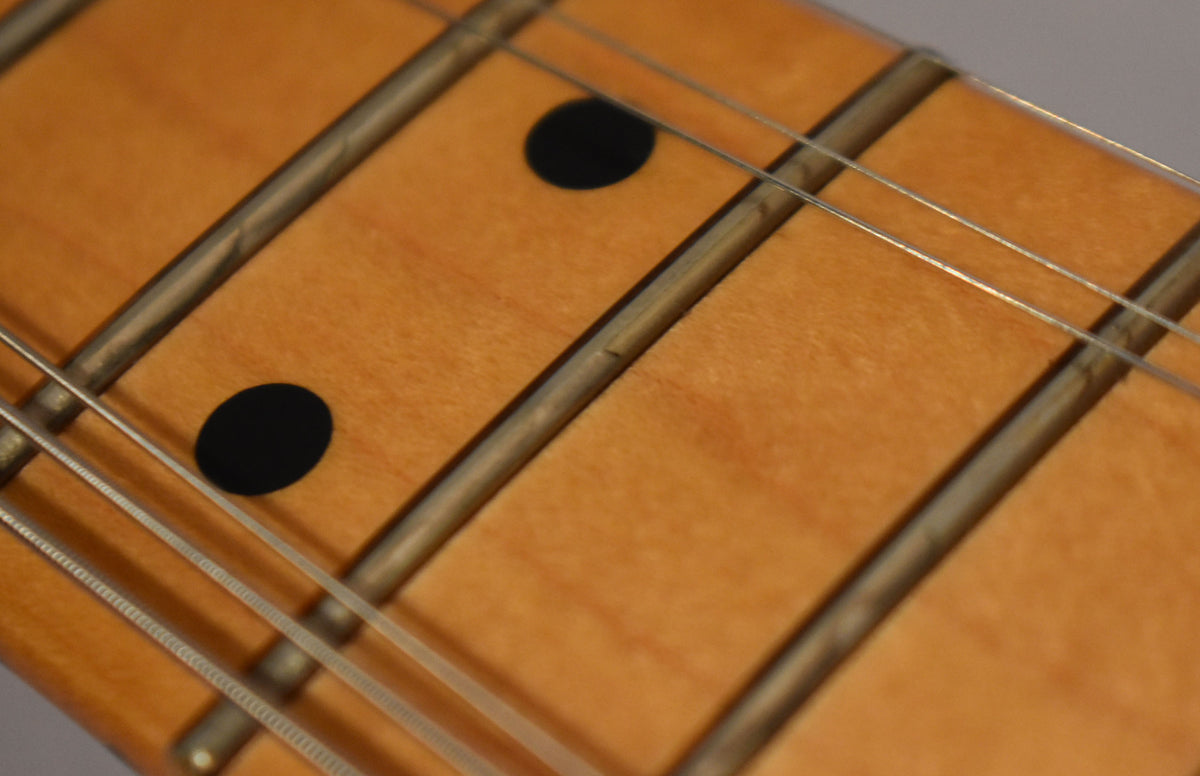 Close-up of the maple fretboard, showing two black dot inlays and four strings over worn frets.