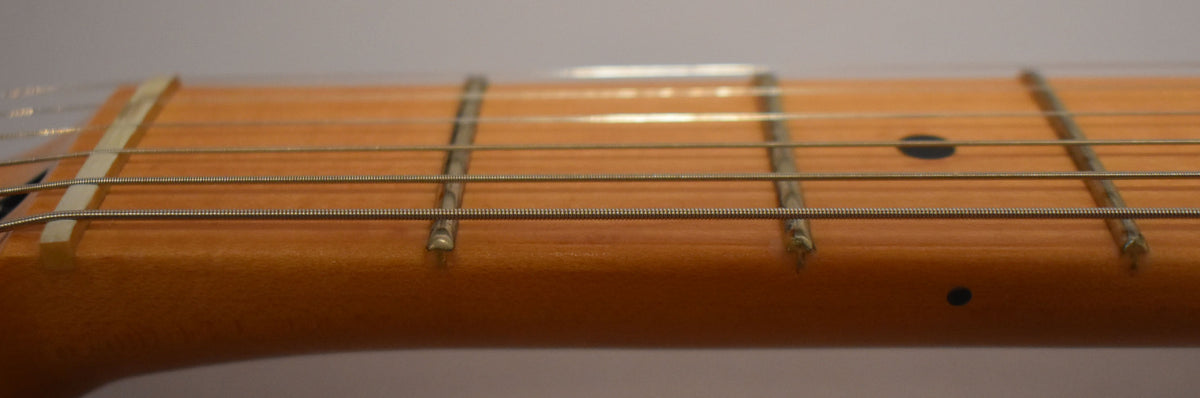 Close-up of the maple fretboard, showing the nut, first four frets, strings, and black dot inlays.