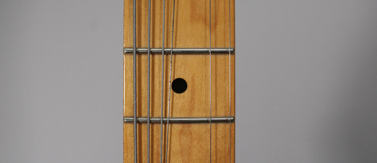 Close-up of the maple fretboard, showing the 7th fret with a black dot inlay and four strings running over the frets.