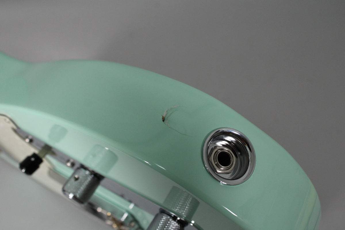 Close-up of the guitar's lower bout, showing the surf green finish, chrome output jack, and a visible chip with finish cracks above it.