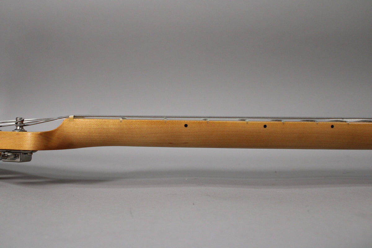 The guitar's light-colored maple neck and fretboard are viewed from the side, showing the first few frets and black dot inlays.