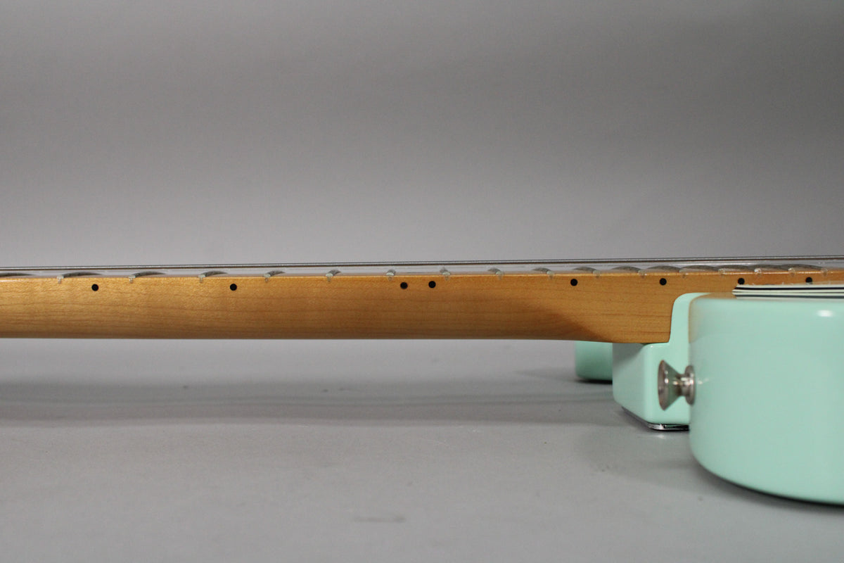 The guitar's light maple neck and fretboard are seen from the side, joining the surf green body with a chrome strap button.