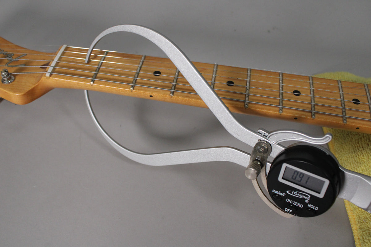 A close-up of the guitar's maple fretboard with black dot inlays, showing a digital caliper measuring fret height at 0.91mm.