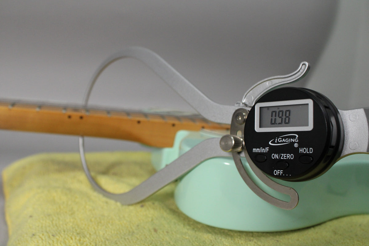 A digital caliper measures the neck relief of the Surf Green Telecaster, showing "0.98" on its screen.