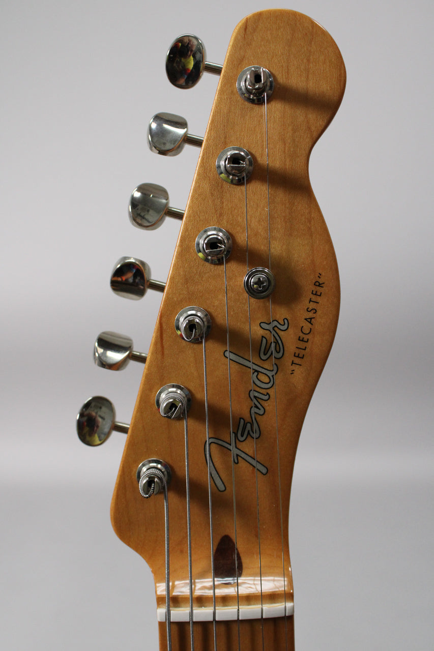 Close-up of the guitar's headstock, angled left, showing six chrome tuners on a light wood finish, with strings wrapped around them.