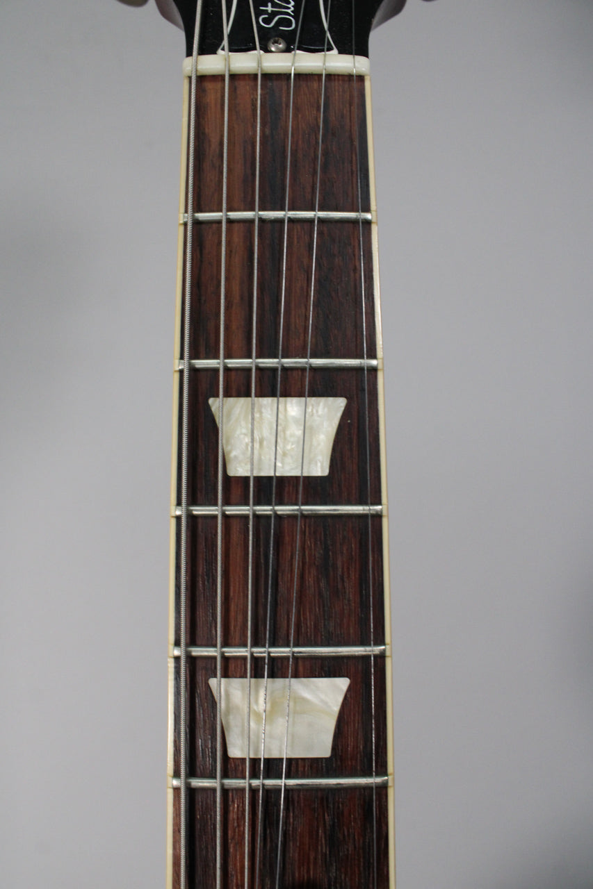 Close-up of the dark rosewood fretboard with trapezoid mother-of-pearl inlays, showing the frets and strings.