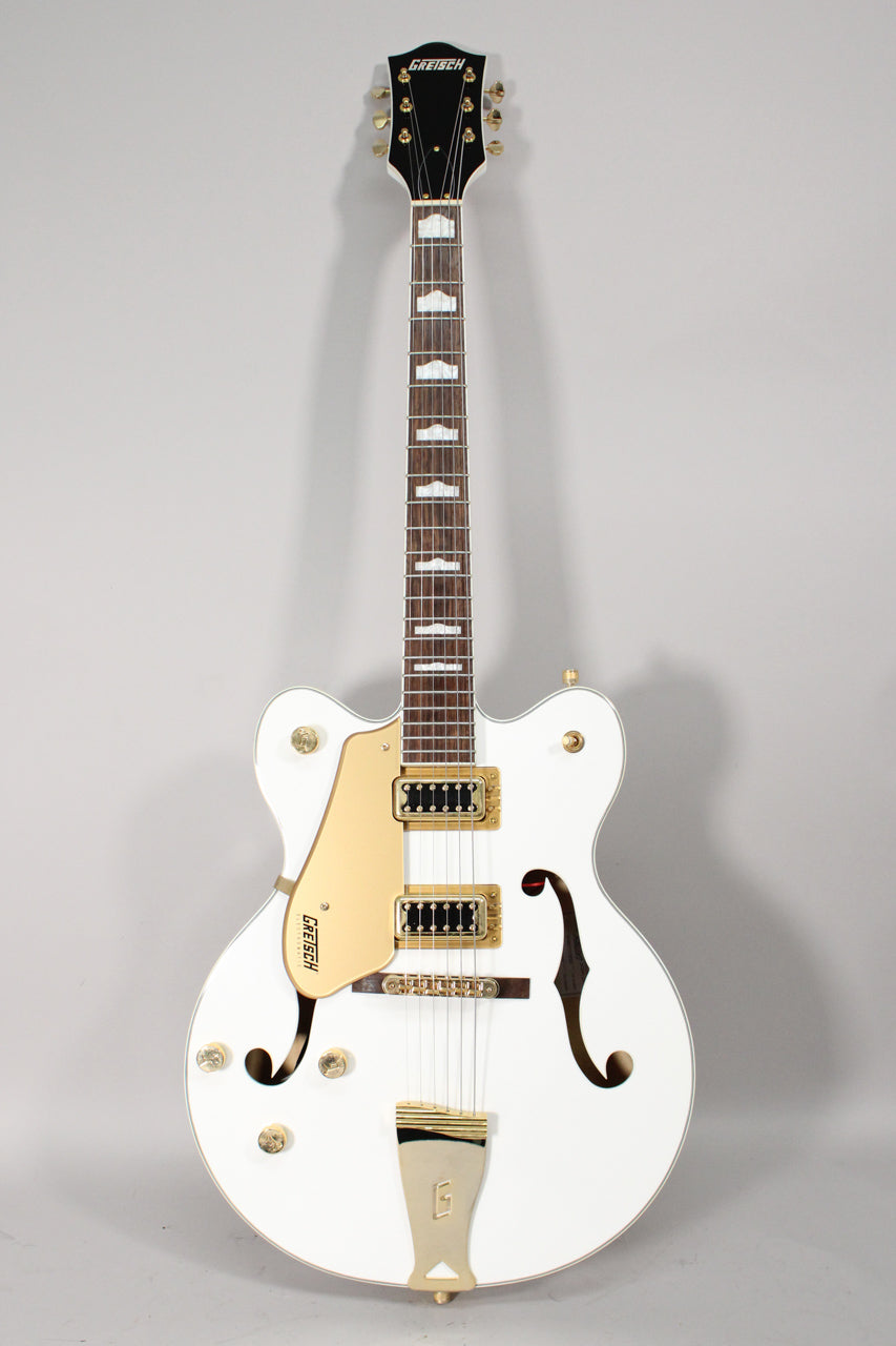 Full-length view of a white hollow body electric guitar with gold hardware, f-holes, and a gold pickguard.