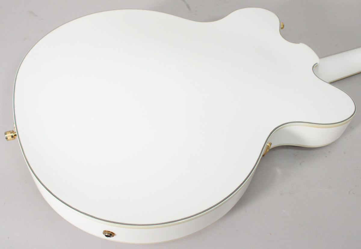 The back of a white hollow body electric guitar with gold strap buttons and binding, angled from the lower left.